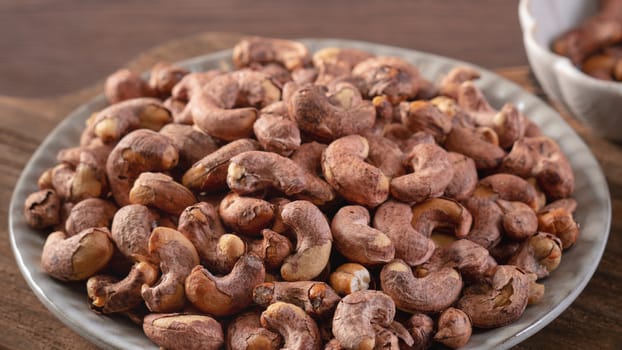 Cashew nuts with peel in a plate on wooden tray and table background, healthy raw food concept.