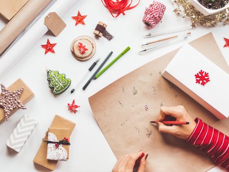 Top view on table with Christmas decorations. Woman draws New Year symbols on craft paper and wraps presents. Flat lay.