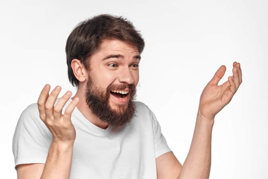 cheerful bearded man in a white t-shirt emotions gestures with his hands light background studio. High quality photo