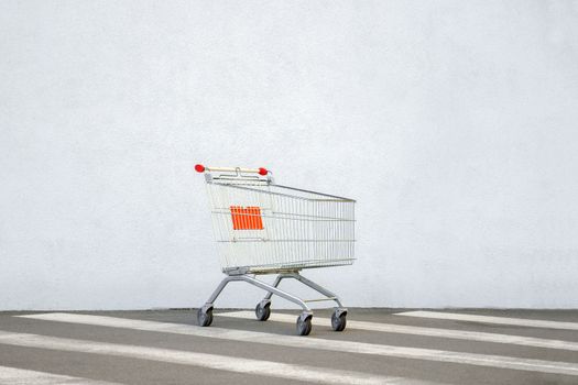 Empty Shopping Cart Trolley Stands near Mall with Copy Space. Grocery Cart on the White Wall Store. Trolley at the Supermarket. E-commerce. Shopping Concept. Side View. Shopping Online. Black Friday