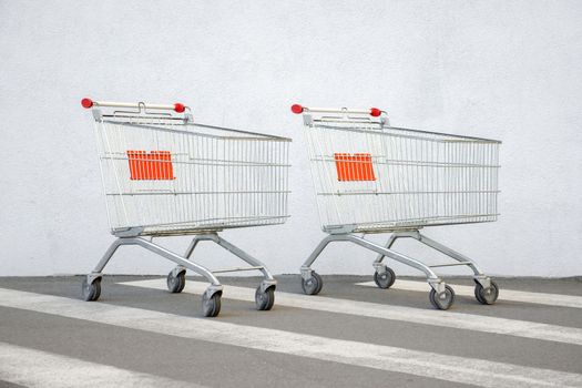 Two Empty Shopping Cart Trolley Stands near Mall with Copy Space. Grocery Cart on the White Wall Store. Trolley at the Supermarket Background. E-commerce. Shopping Concept. Side View. Shopping Service