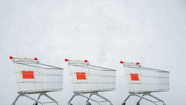 Three Empty Shopping Cart Trolley Stands near Mall with Copy Space. Grocery Cart on the White Wall Store. Trolley at the Supermarket. E-commerce. Shopping Concept. Side View. Black Friday Sale. Online
