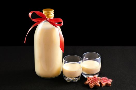 Homemade eggnog in bottle and two glasses with Christmas cookies on dark background
