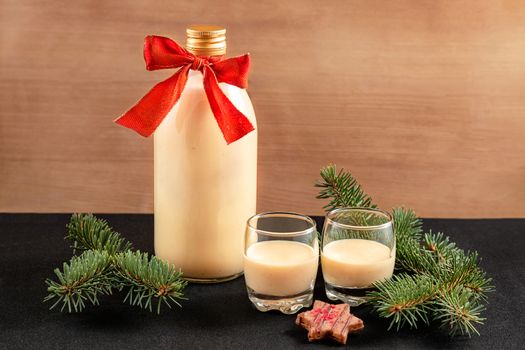 Homemade eggnog in bottle and two glasses with Christmas decoration on wooden background