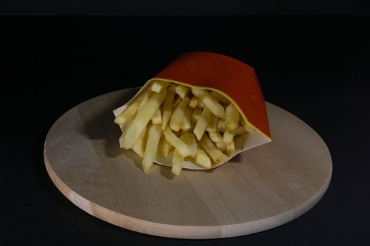 French fries on a black background on a wooden board in a red and yellow package