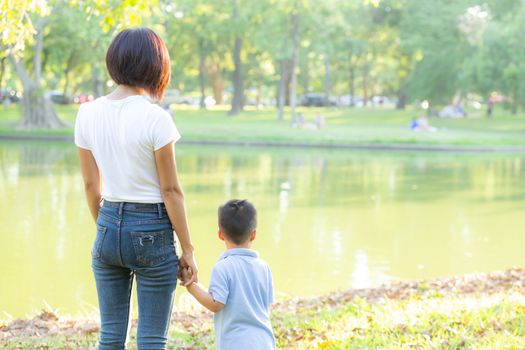 Asian mother or parent and son holding hand with love together in summer outside in the park, mom take care kid holding palm with affection, child have a trust for mother, family concept.
