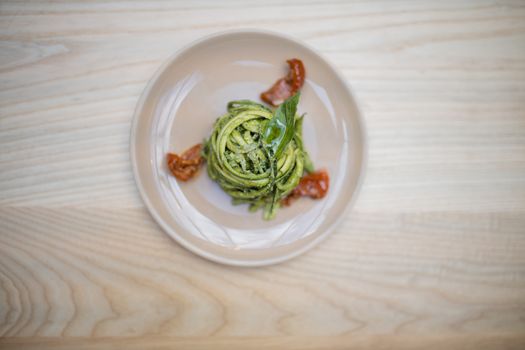 Above view of tasty looking zucchini noodles with a spinach leaf on top and on a wooden restaurant table