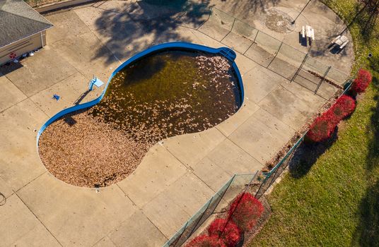 Aerial drone point of view of an uncovered swimming pool filled with fallen leaves in the autumn after wind and storms