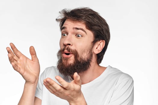 cheerful bearded man in a white t-shirt emotions gestures with his hands light background studio. High quality photo