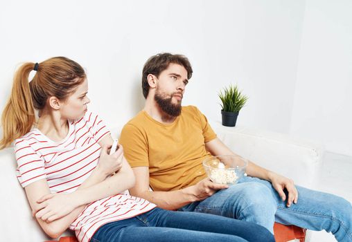 A woman in a striped T-shirt and a man on the couch watching the TV in a bright room. High quality photo
