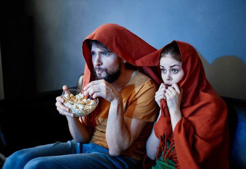 scared woman with a red plaid on her head and a man with a plate of popcorn in a dark room. High quality photo