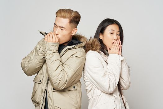 A man and a woman in winter jackets coolness warm their hands gray background