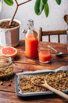 Homemade muesli on baking sheet with wooden spoon, grapefruit juice and sliced fruit