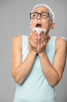 Senior women with short gray hair coughs and sneezes into a handkerchief, studio shoot, allergies and illness concept