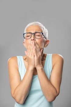 Pain - hands on mouth. Senior women with short gray hair and glasses coughs and sneezes into a handkerchief, studio shoot, allergies and illness concept