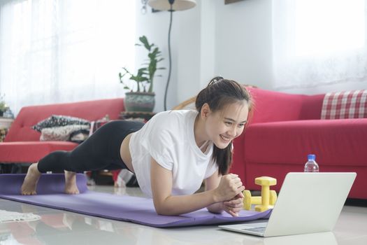 Fit woman doing yoga plank and watching online tutorials, training in living room. Stay at home life style.