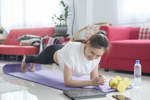 Fit woman doing yoga plank and watching online tutorials, training in living room. Stay at home life style.