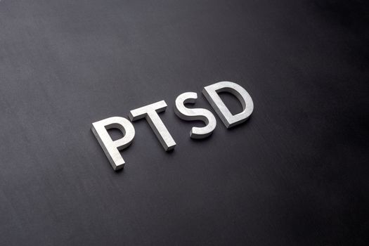 the word PTSD - post traumatic stress disorder - laid with silver metal letters on flat black background in linear perspective with selective focus