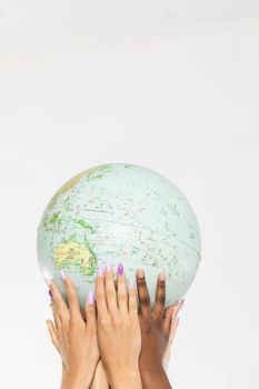 A large globe with all continents is supported by female hands of various races, symbolizing unity, acceptance and racial tolerance.