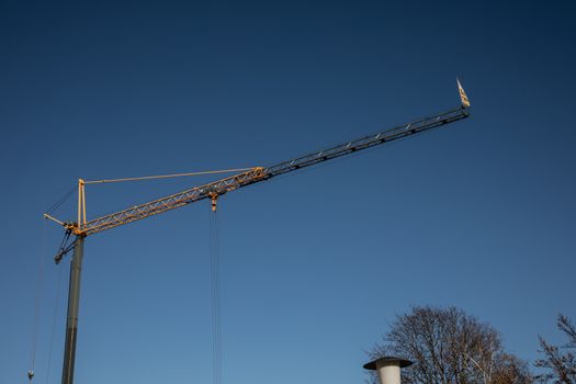 yellow crane with long boom at construction site against a blue sky