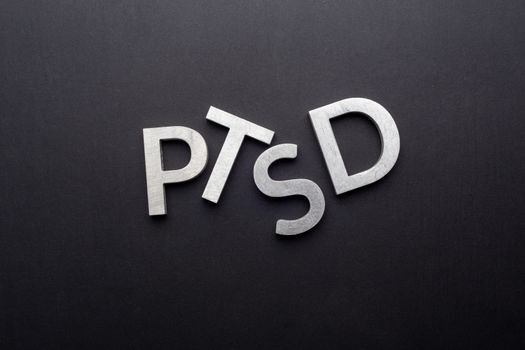 the word PTSD - post traumatic stress disorder - laid with silver metal letters on flat black background in directly above perspective
