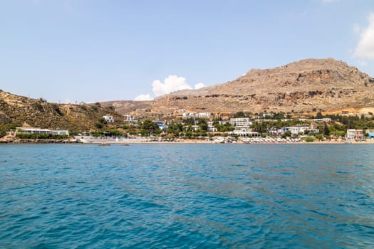 View from a boat on the water at Stegna beach with the mediterranean sea in the foreground and mountain range in the background on a sunny day in spring