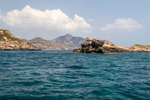 View from a motor boat on the mediterranean sea at the rocky coastline near Stegna on the eastside of Greek island Rhodes on a sunny day in spring