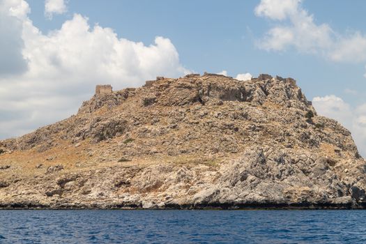 View from a motor boat on the mediterranean sea at the rocky coastline near Lindos  on the eastside of Greek island Rhodes with ruins of a castle on the top of a mountain