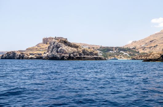 View from a motor boat on the mediterranean sea at the rocky coastline near Lindos on the eastside of Greek island Rhodes on a sunny day in spring