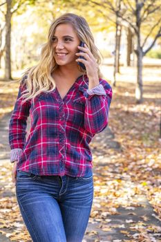 A gorgeous blonde model talks on her cellphone on an autumn day outdoors in a park