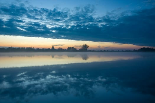 Reflection of the evening clouds in a misty lake, october view