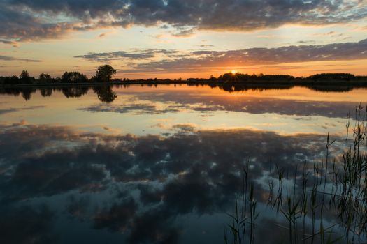 Beautiful sunset over a calm lake and reflection of clouds in the water, summer view