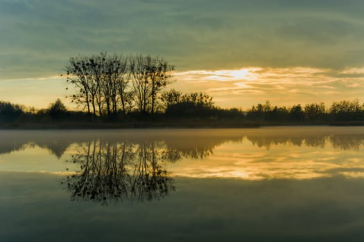 Reflection of evening clouds and trees in a misty lake, october view