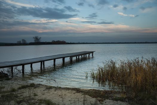 Wooden pier and reeds on the shore of the lake, evening view