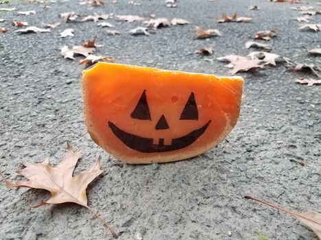 orange cheese with pumpkin face on asphalt with leaves