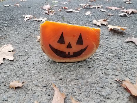 orange cheese with pumpkin face on asphalt with leaves