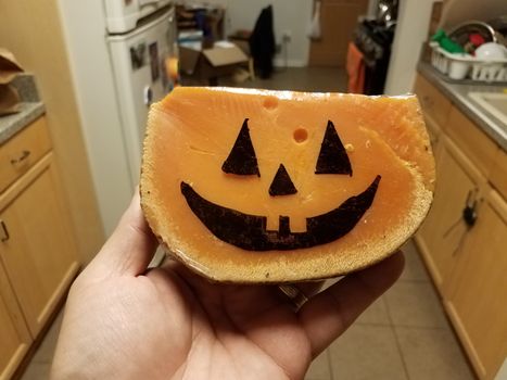 hand holding orange cheese with pumpkin face in kitchen