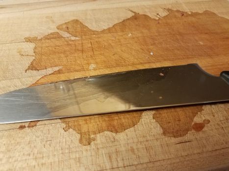 sharp metal knife on wood cutting board with stain