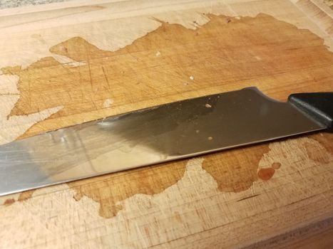 sharp metal knife on wood cutting board with stain