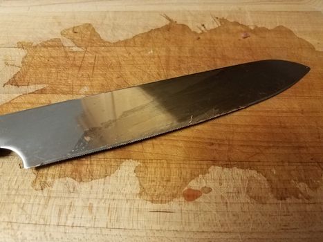 sharp metal knife on wood cutting board with stain