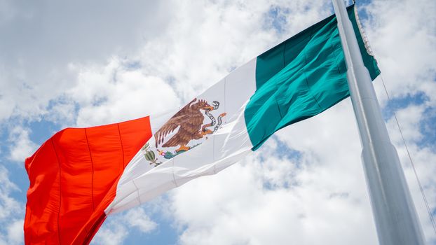 Low Angle Picture of the Mexican Flag Waving in the Wind and a Slightly Cloudy Blue Sky as the Background
