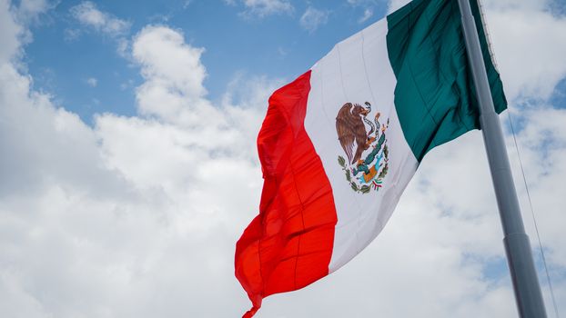 Picture of the Mexican Flag Waving in the Wind and a Slightly Cloudy Blue Sky as the Background