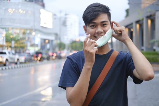 Young man during pandemic isolation at city. Removing mask from face. Coronavirus and New normal concept.