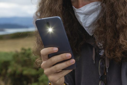 A young woman, wearing a protective face mask, takes a photograph with a smart mobile phone, Spain.