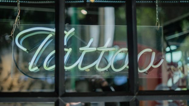 Picture of a blue Tattoo light sign on a window from barber shop and tattoo studio