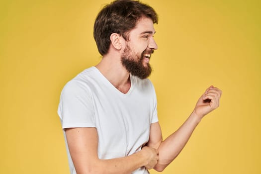 Bearded man white t-shirt emotions gestures with hands fun yellow background. High quality photo
