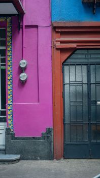 Portrait style picture of the front side of a pink house and an orange and blue house next to each other