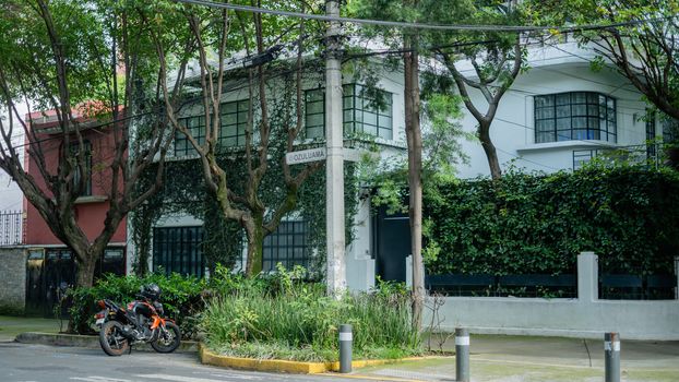 Picture of a large white house from the Coyoacan neighbourhood with a motorcycle parked outside