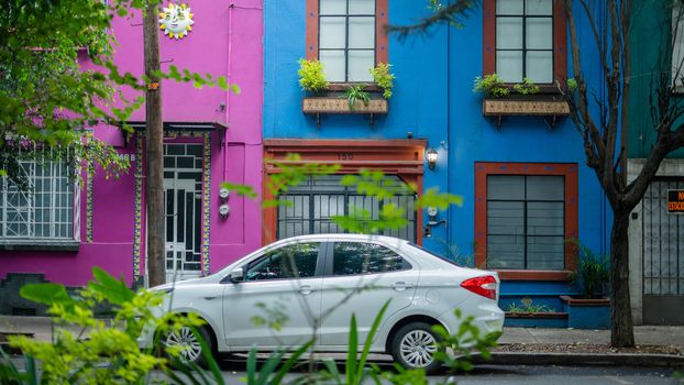 Picture of a white car parked outside a blue and a pink house