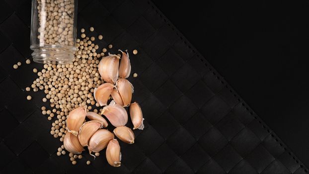 Natural Garlic and white peppercorn in glass bottle on plate mat black background in studio shot. It is main ingrediant for many asian recipe menu such as Singapore Bak kut teh, Thailand’s Pad Thai and more.